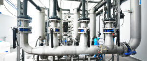 Large industrial water treatment and boiler room. Shiny steel metal pipes and blue pupms and valves.